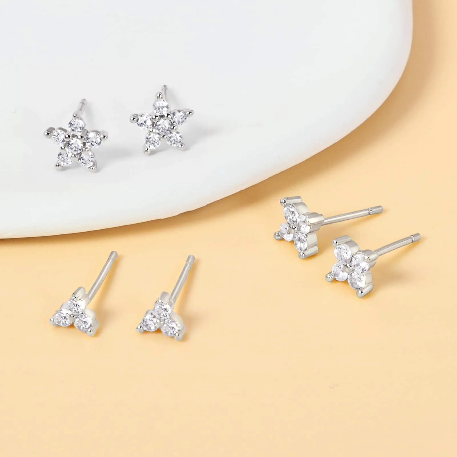 Two silver star-shaped studs on a white disc and three plain clear studs lying on peach paper beside them