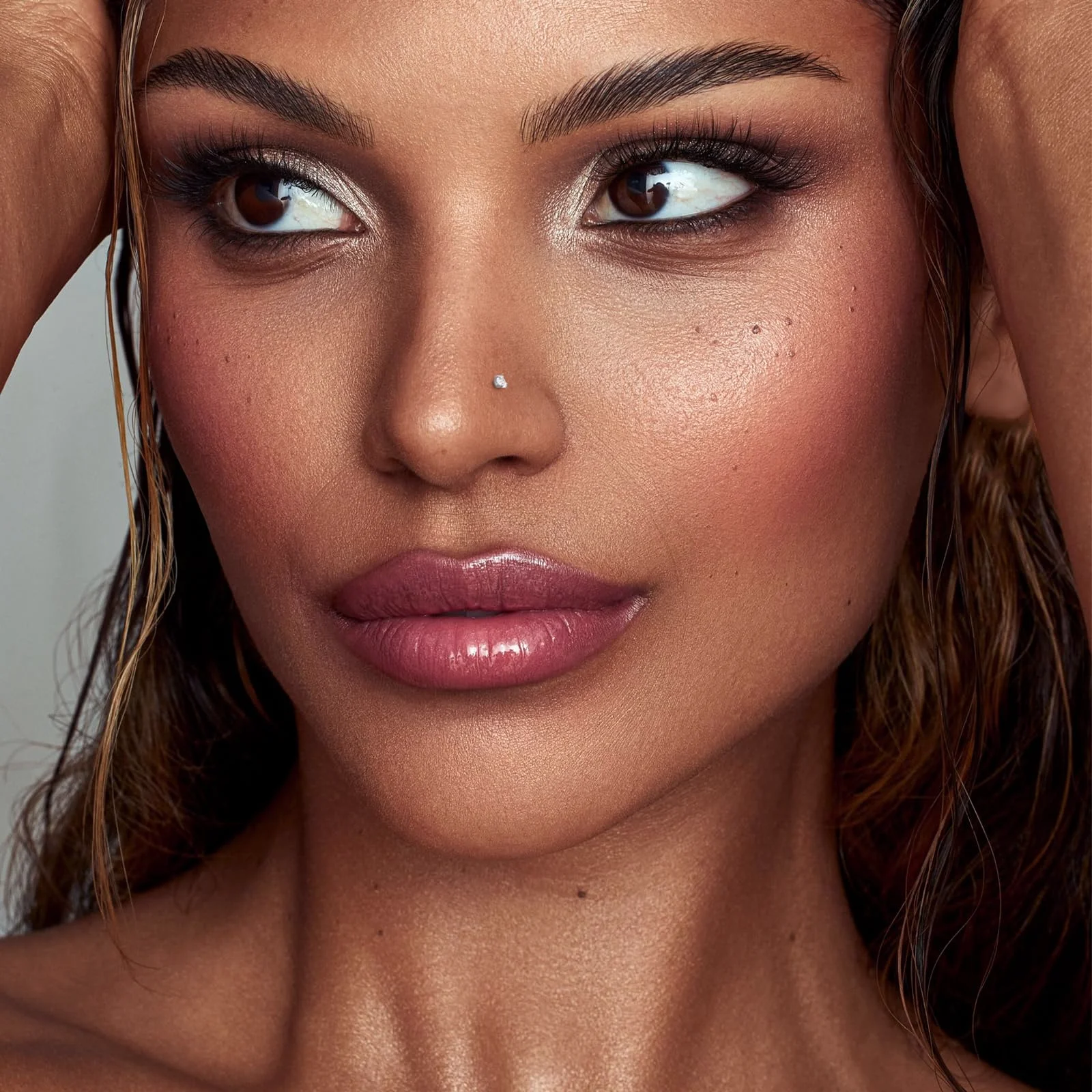 A close portrait in strong make-up with wet hair, a small clear stud in the nostril and the eyes turned away from the camera