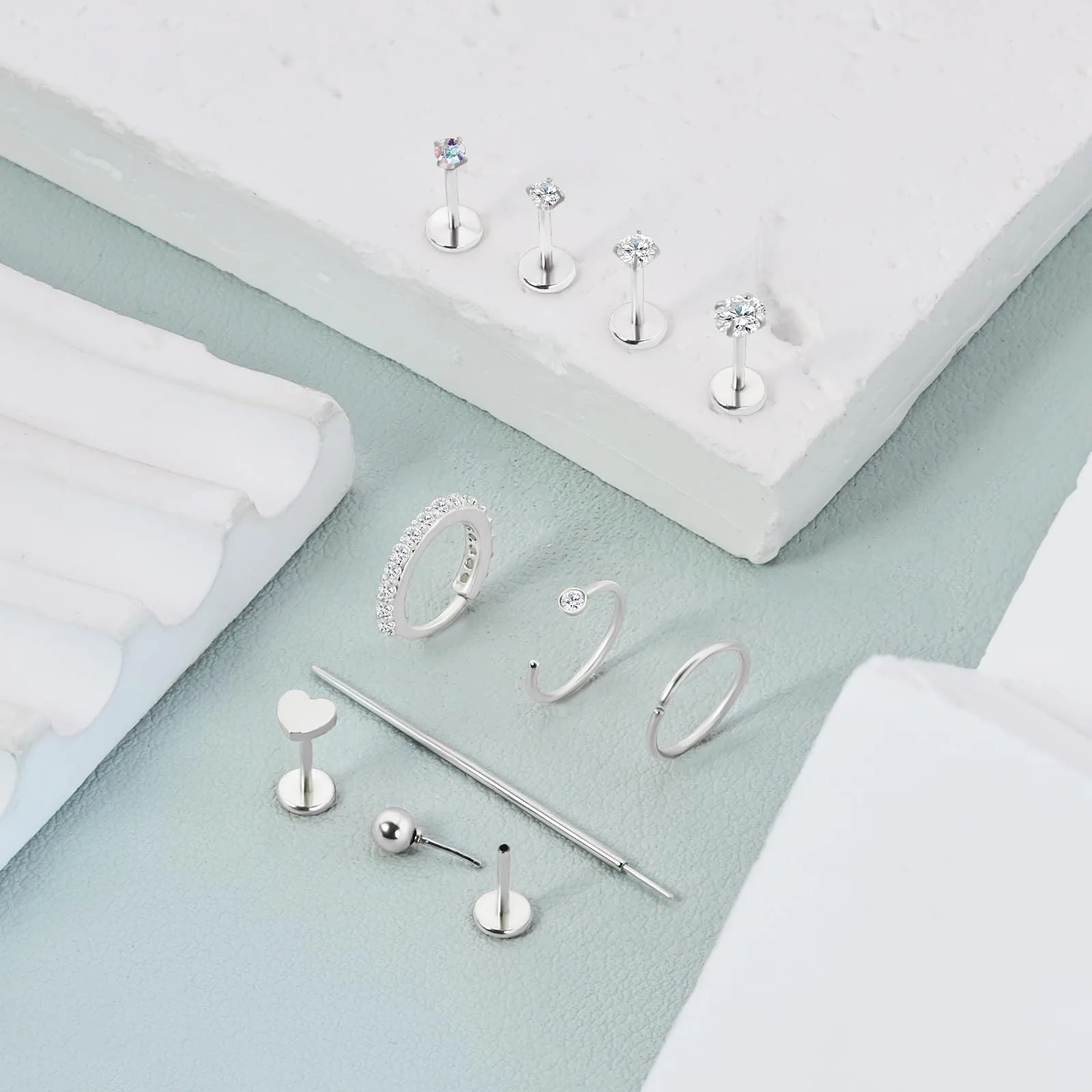 Silver flat backs, two paved hoops and a plain barbell arranged on a pale green ground beside a white block