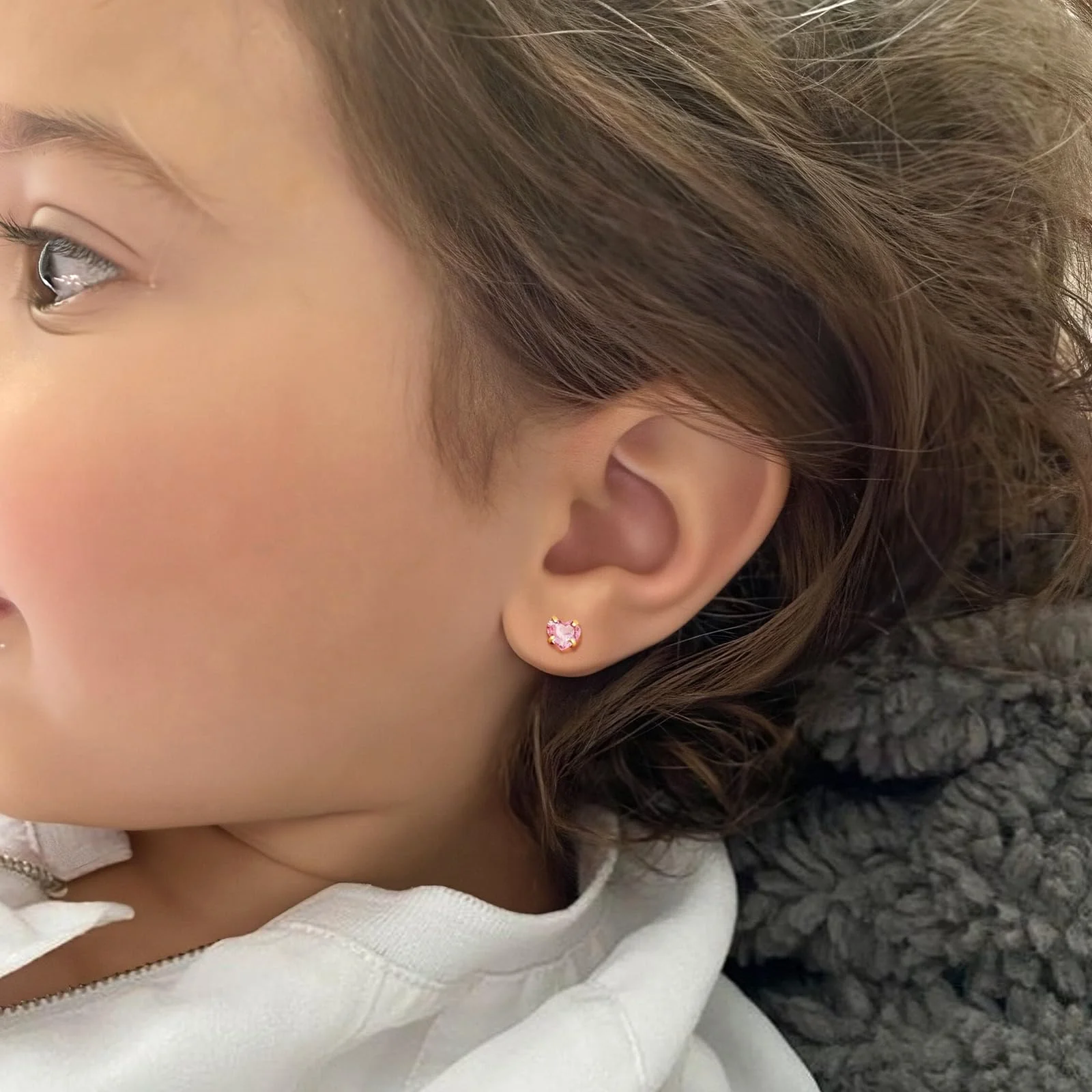 A child in profile with a small pink stone in the lobe, hair pulled back over the ear, a grey fleece collar behind