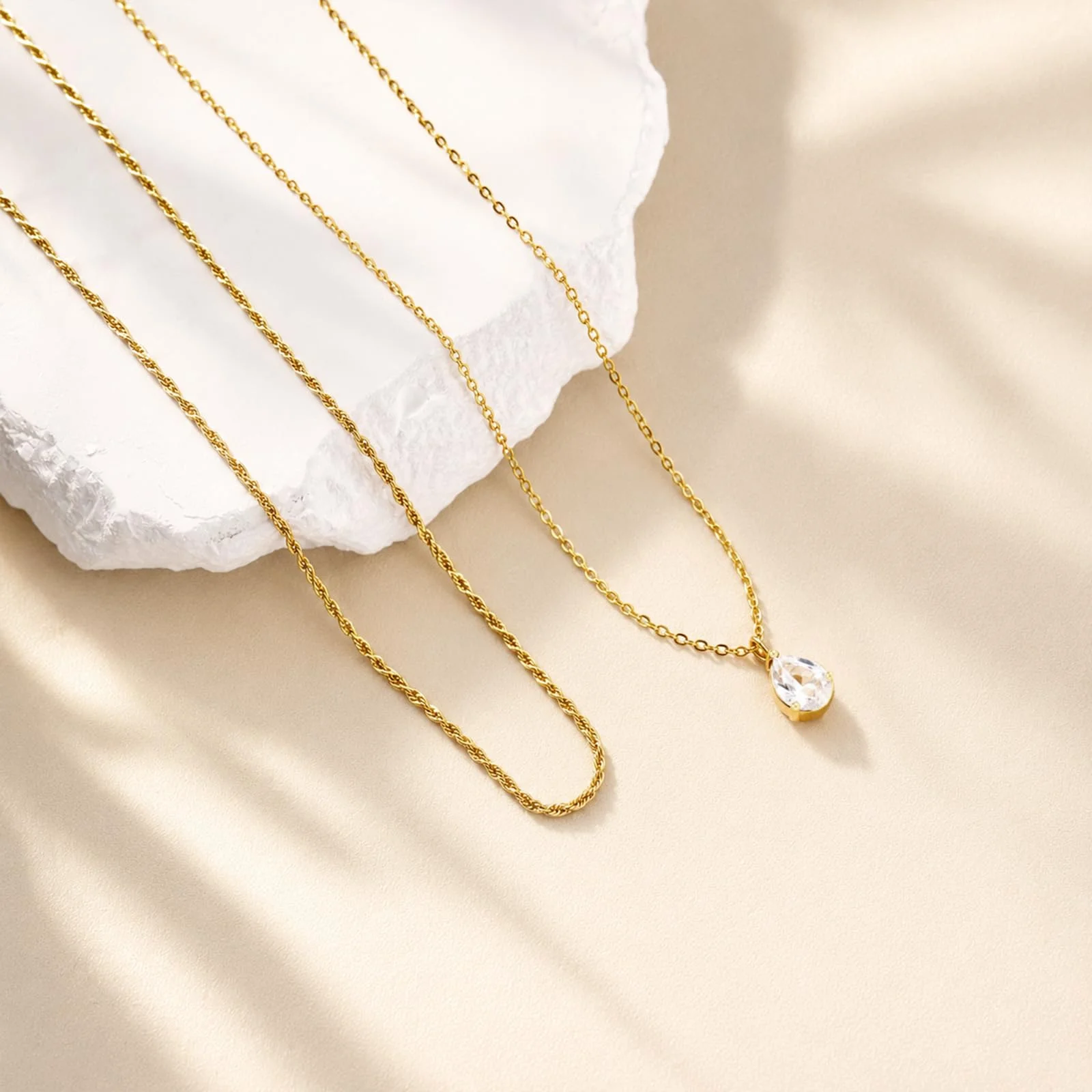 Two fine gold chains over a white stone, the lower one carrying a single teardrop stone, in hard afternoon light